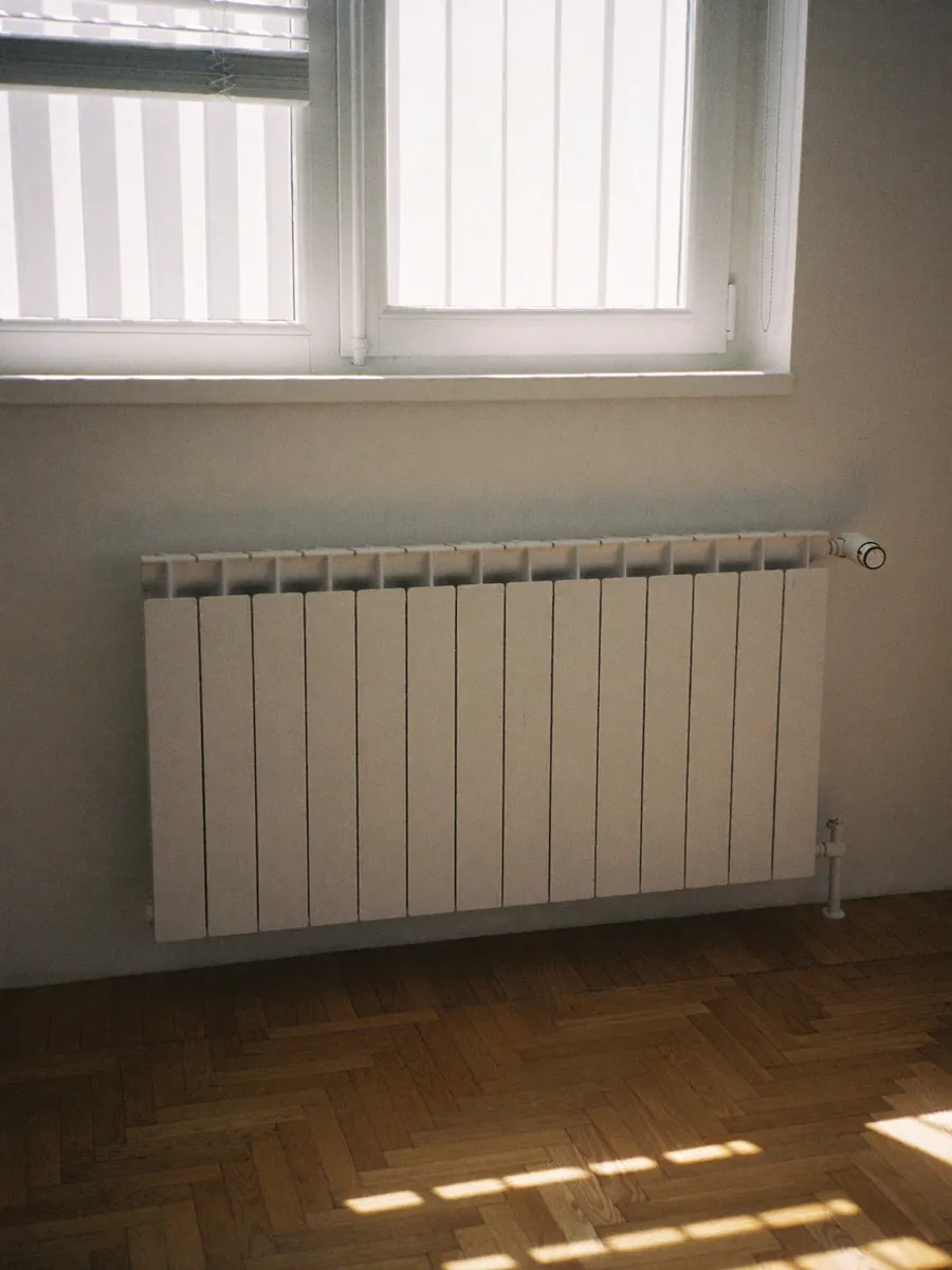 Un radiateur avec sa tête thermostatique sous une fenêtre